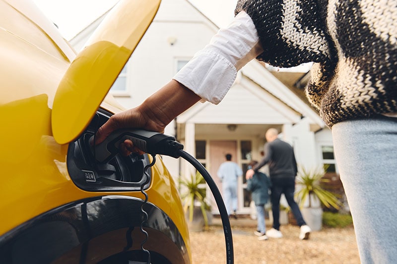 Electric Vehicle Charging Stations. Woman plugging electric charger into car.